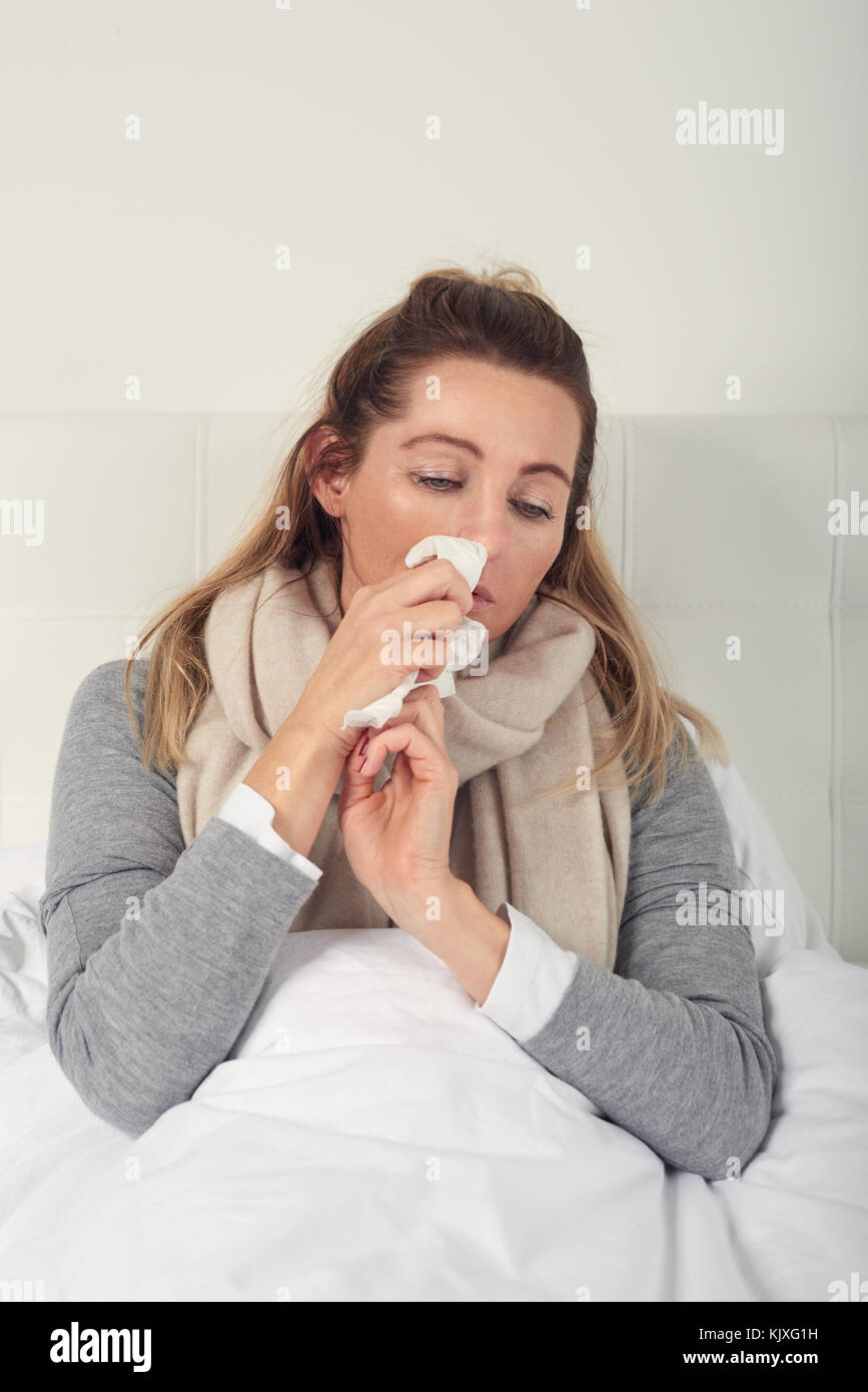 Kranke Frau mit saisonalen Kälte und Grippe liegen, gemütlich im Bett mit einem miserablen Ausdruck ihrer Nase Blasen auf einem Gewebe umwickelt Stockfoto