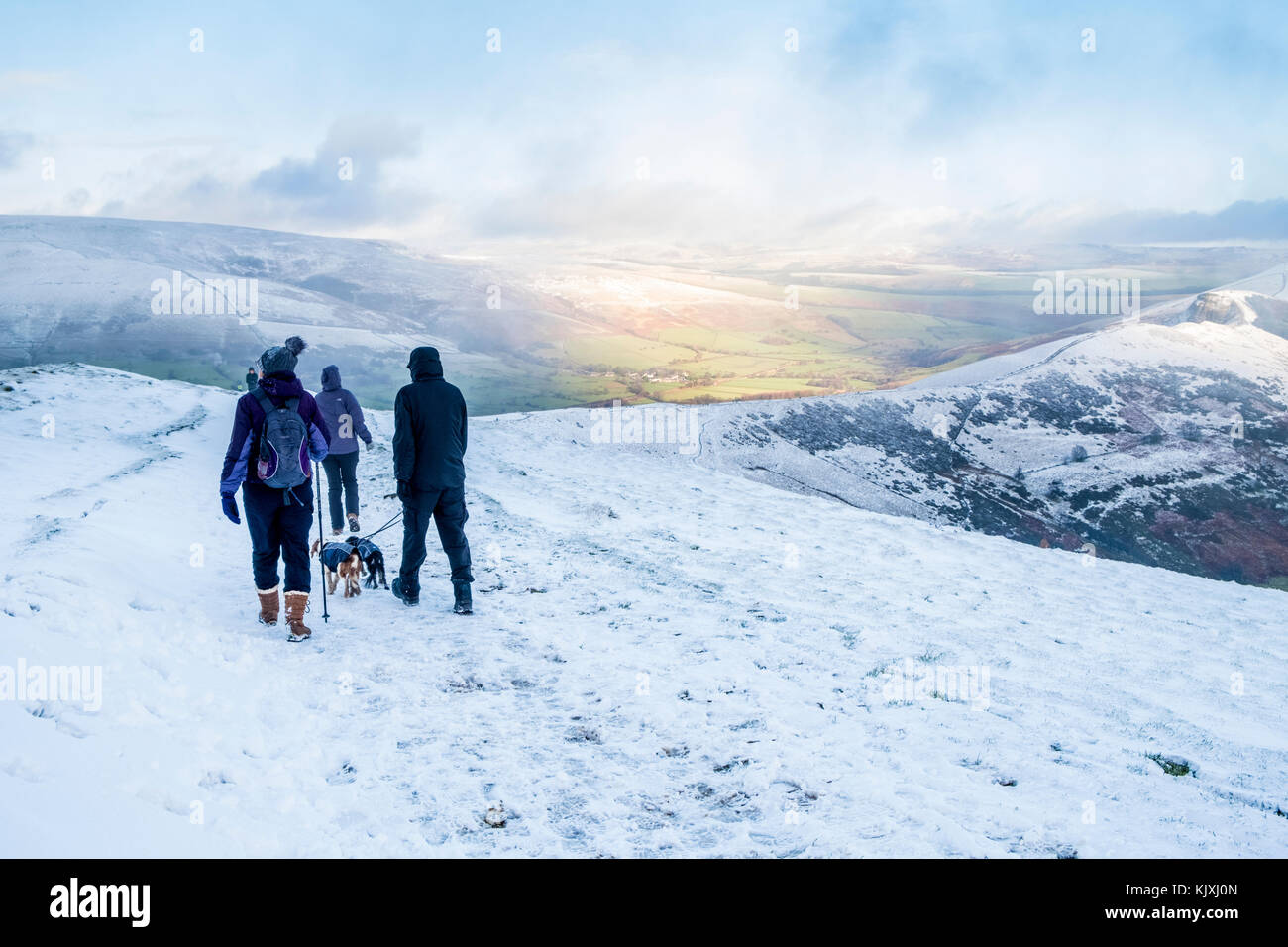 Winter wandern. Wanderer mit Hunden im Schnee auf der großen Ridge, mit Sonne in der Ferne. Peak District, Derbyshire, England, Großbritannien Stockfoto