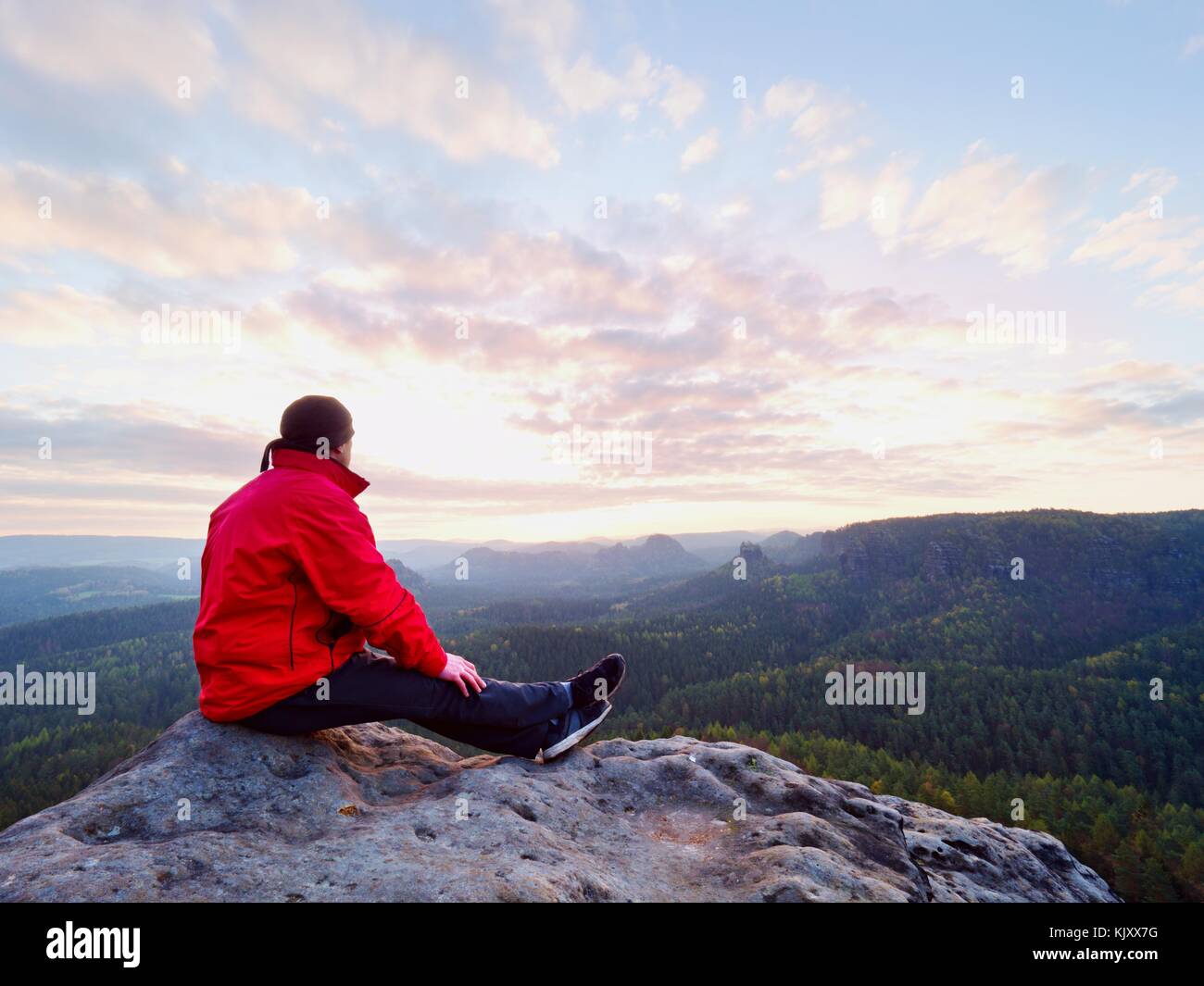 Sitzung Wanderer auf Rock. Mann in Rot Schwarz warme Kleidung sitzt auf Felsen und genießen weit anzeigen. Blick in Misty hügeligen Tal unten Stockfoto