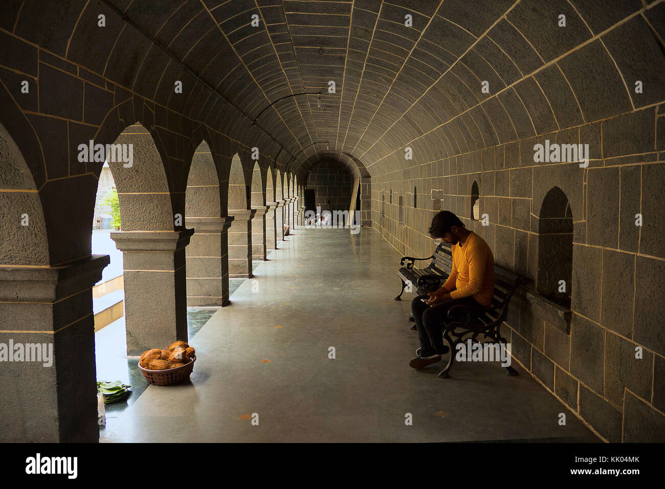 Junger Indianer, der in Orange gekleidet ist und sein Handy überprüft, der auf der Tempelveranda sitzt, Vitthal Mandir, Vithalwadi, Pune Stockfoto