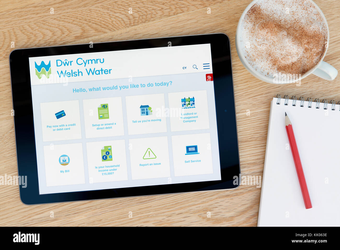 Ein Mann schaut auf die Waliser Wasser Website auf seinem iPad tablet device, Schuß gegen einen hölzernen Tisch top Hintergrund (nur redaktionelle Nutzung) Stockfoto