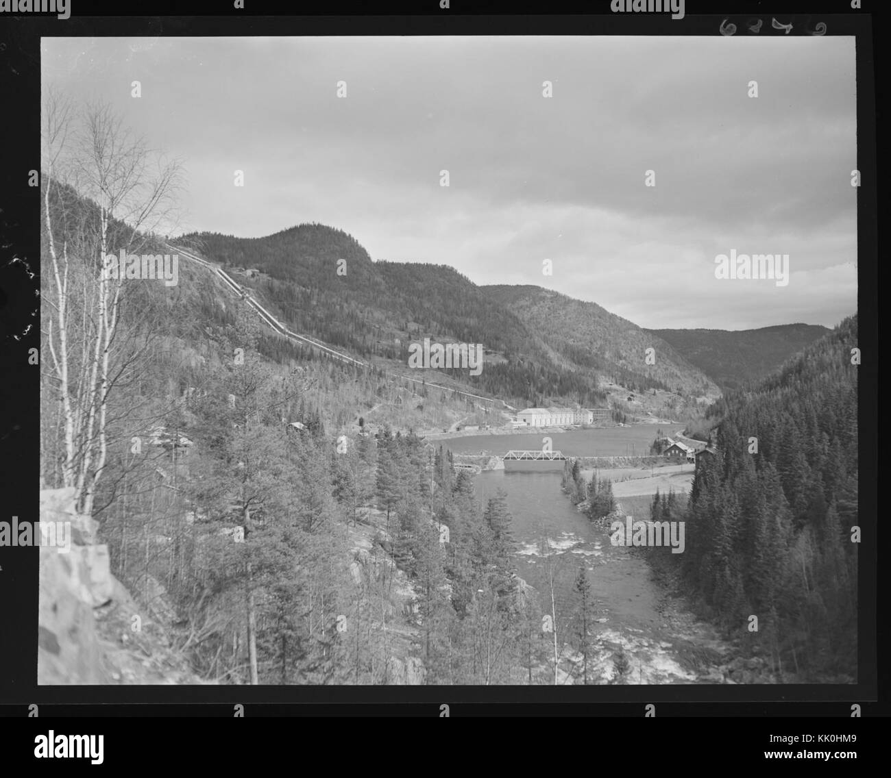 Ein historisches Foto, das ein Kraftwerk in der Nähe eines Flusses in Norwegen zeigt und die Industrielandschaft des frühen 20. Jahrhunderts beleuchtet. Stockfoto