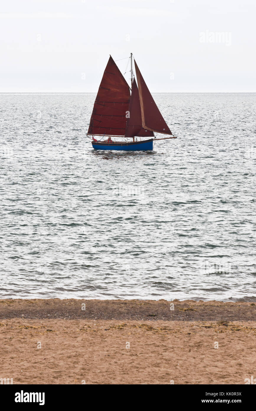 Ein einsamer Segler Segeln in den Eingang des Flusses Exe in Exmouth auf der South Devon Coast auf einen ruhigen Sommer Tag mit all seinen Segel Stockfoto