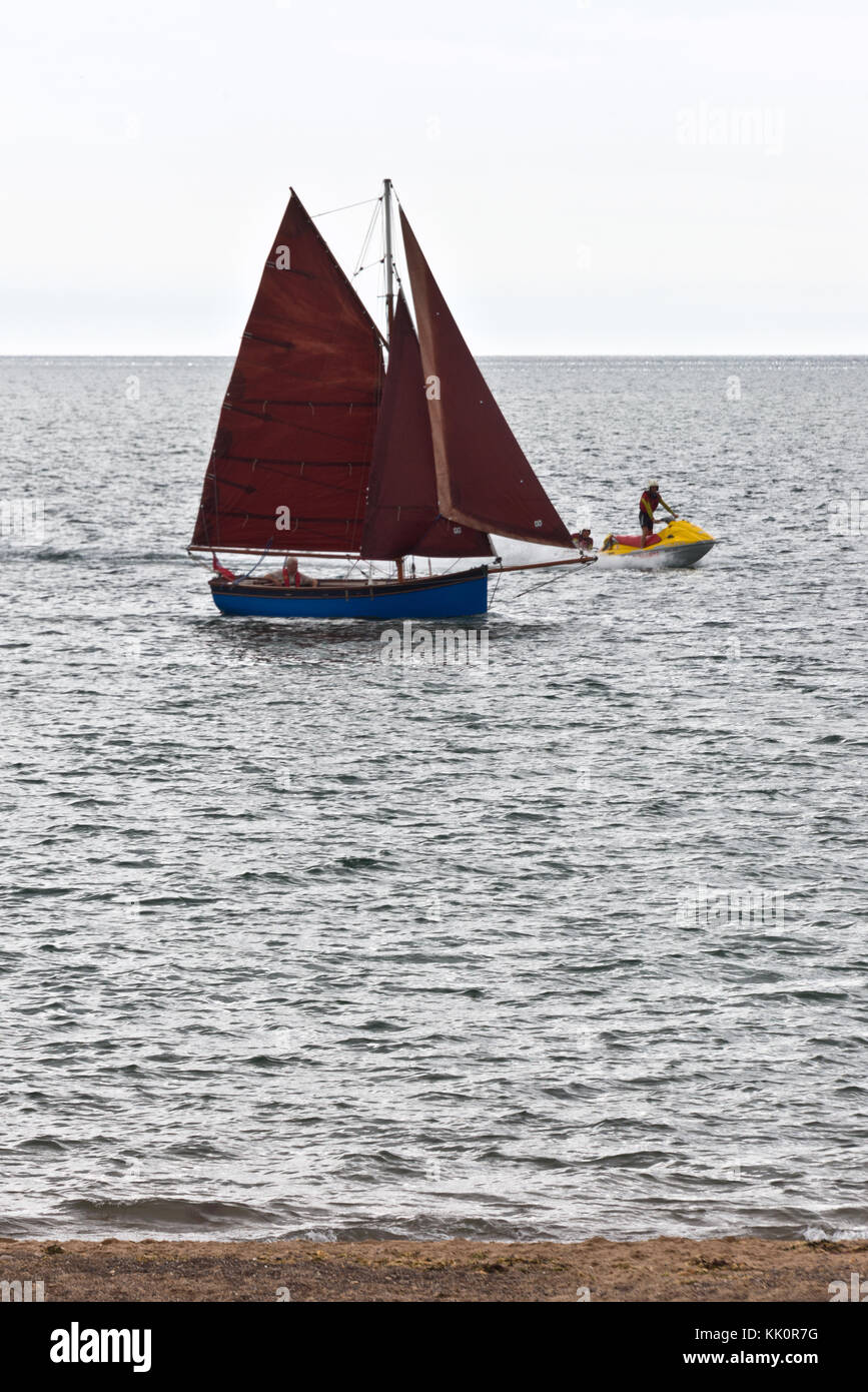 Ein einsamer Segler Segeln in den Eingang des Flusses Exe in Exmouth auf der South Devon Coast auf einen ruhigen Sommer Tag mit all seinen Segel Stockfoto