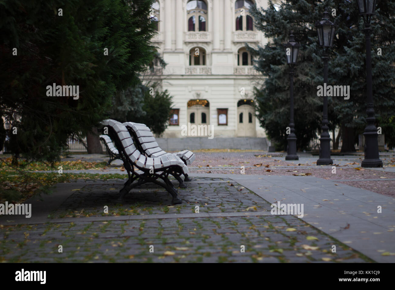 Leere weiße Bank auf eine Herbstlandschaft Park auf der Slowakei Kosice mit einem Gebäude Sehenswürdigkeit auf dem Hintergrund Stockfoto