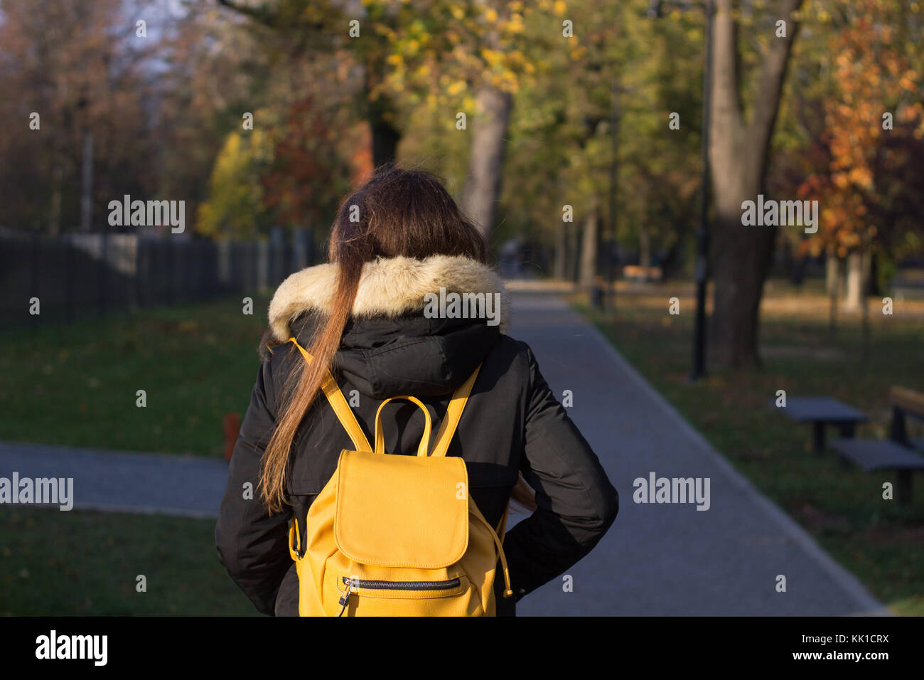 Mädchen mit Rucksack zu Fuß an einem Park mit Jacke und Gelber Sack hinter Foto von hinten Stockfoto