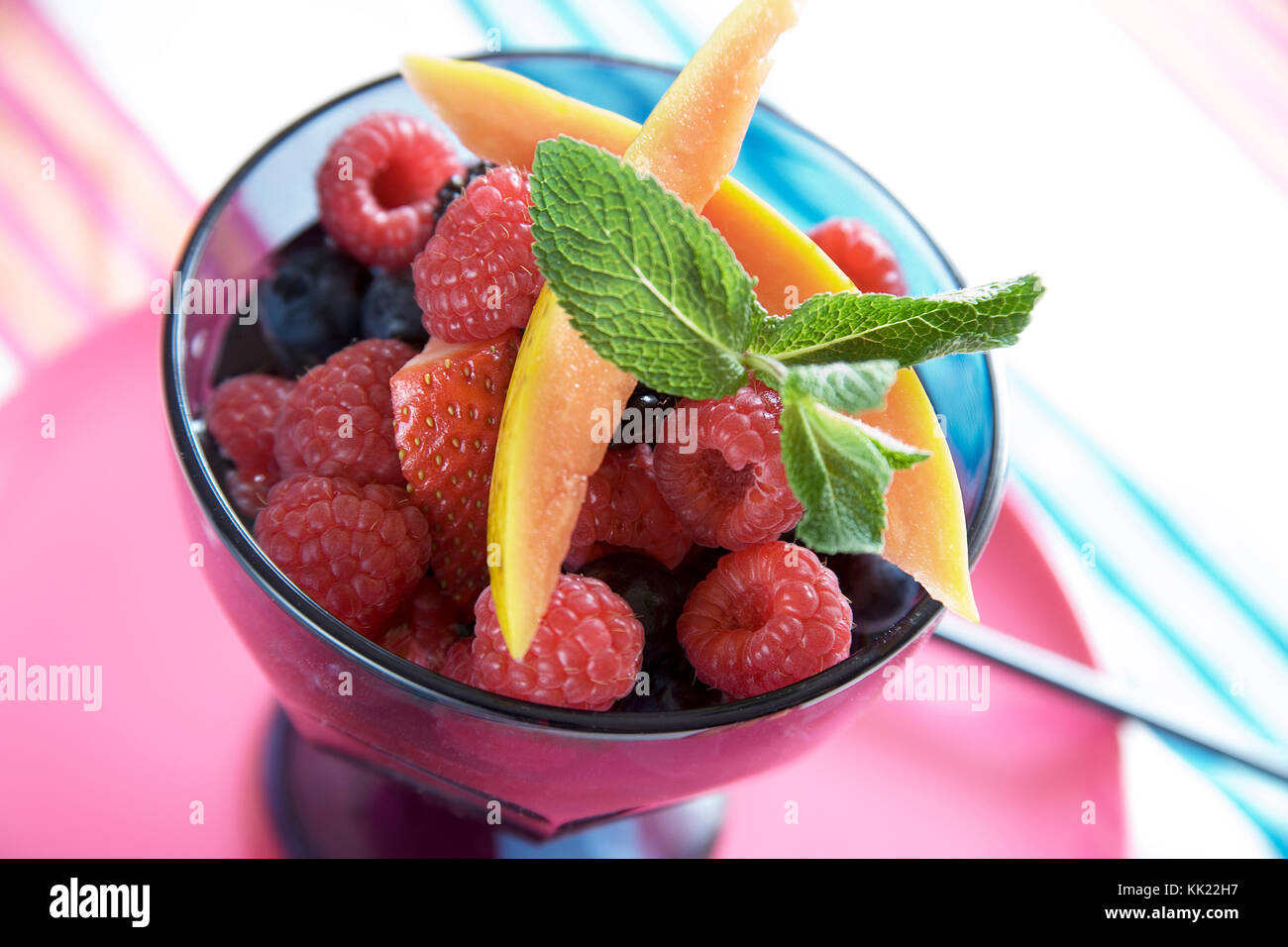 Himbeere, Erdbeere, Heidelbeere und Mango Salat von frischen Früchten garniert mit frischer Minze im Glas Schüssel auf bunte Tischdecke. Stockfoto