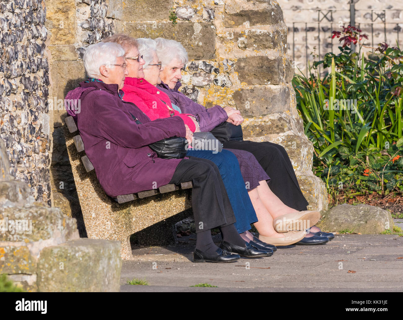 Gruppe von 4 älteren Frauen draußen sitzen auf einer Bank in warme Kleidung im Herbst in Großbritannien. Stockfoto
