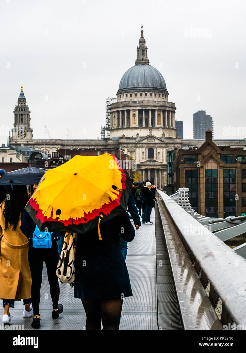 Menschen zu Fuß über die Millennium Bridge an regnerischen Tag mit hellen Sonnenschirmen für die St Paul's Cathedral und die City von London Schule, Themse, England, Großbritannien Stockfoto