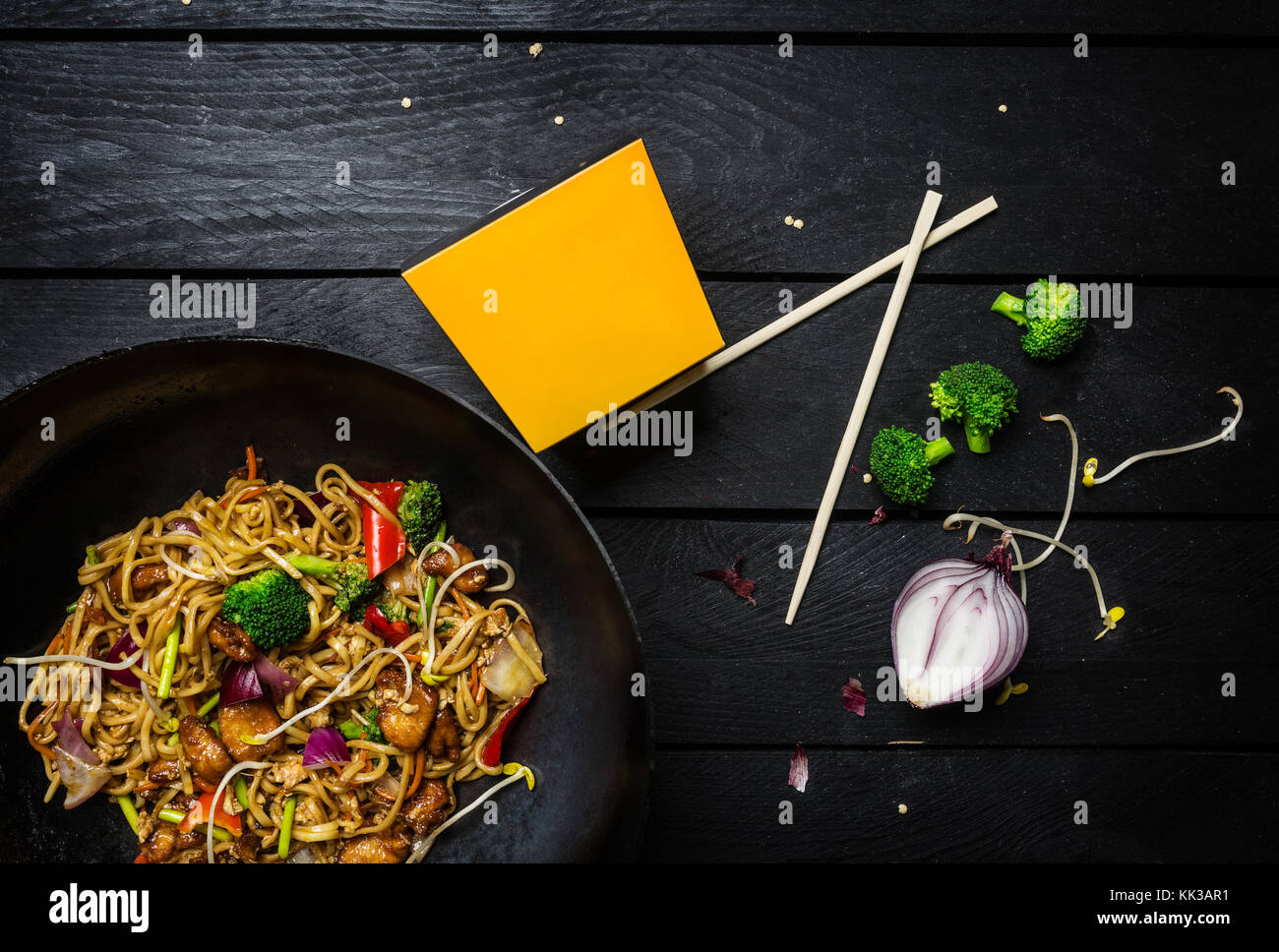 Wok. udon fry Nudeln mit Huhn und Gemüse im Wok rühren Pan auf schwarzem Holz- Hintergrund. Mit einer Box für Nudeln Stockfoto