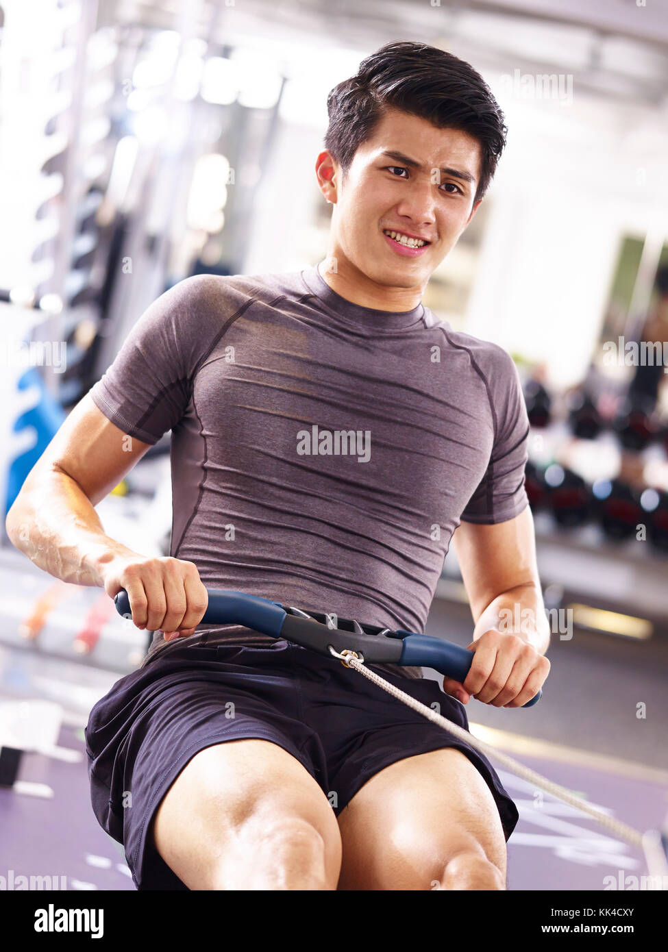 Jungen asiatischen erwachsener Mann heraus in der Turnhalle mit Rudergerät. Stockfoto