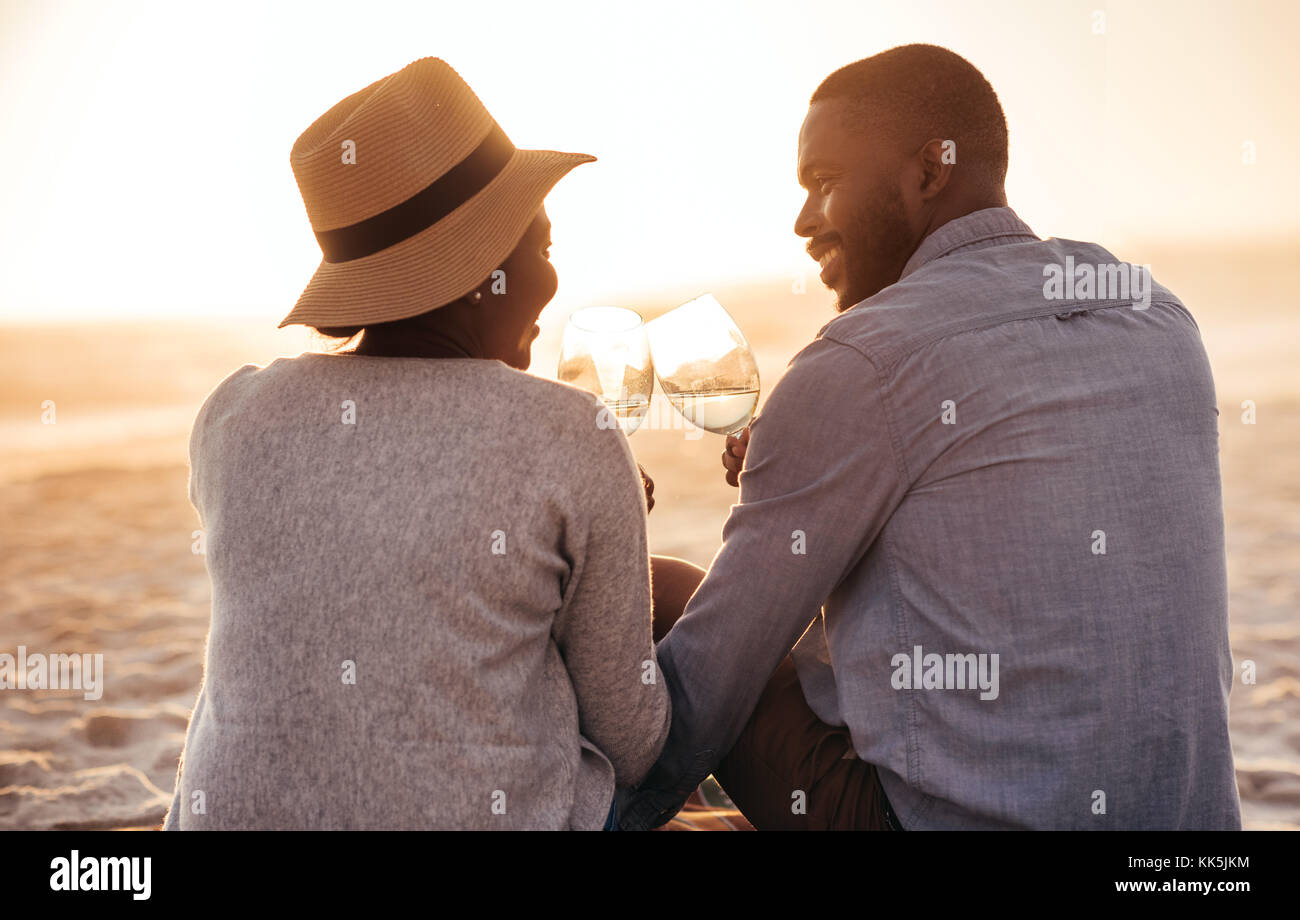 Junge afrikanische Paar Wein trinken und beobachten den Sonnenuntergang am Strand Stockfoto