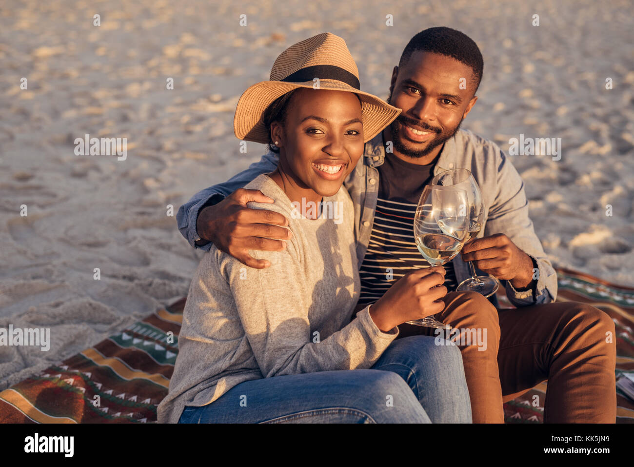 Lächelnden jungen afrikanischen Paar am Strand Wein trinken Sitzen Stockfoto