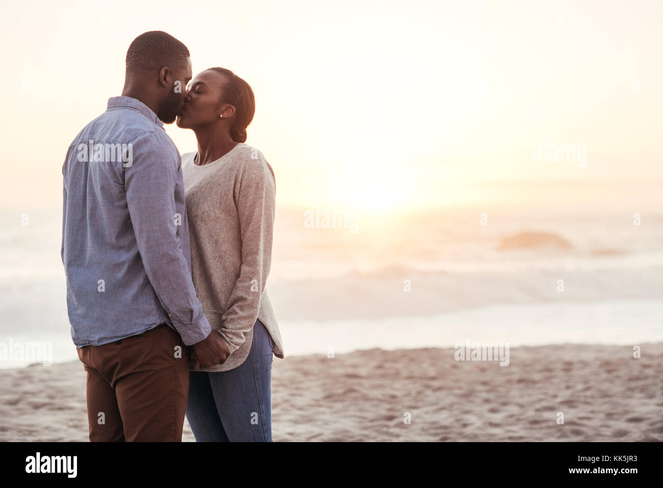 Romantische junge afrikanische Paar küssen am Strand bei Sonnenuntergang Stockfoto