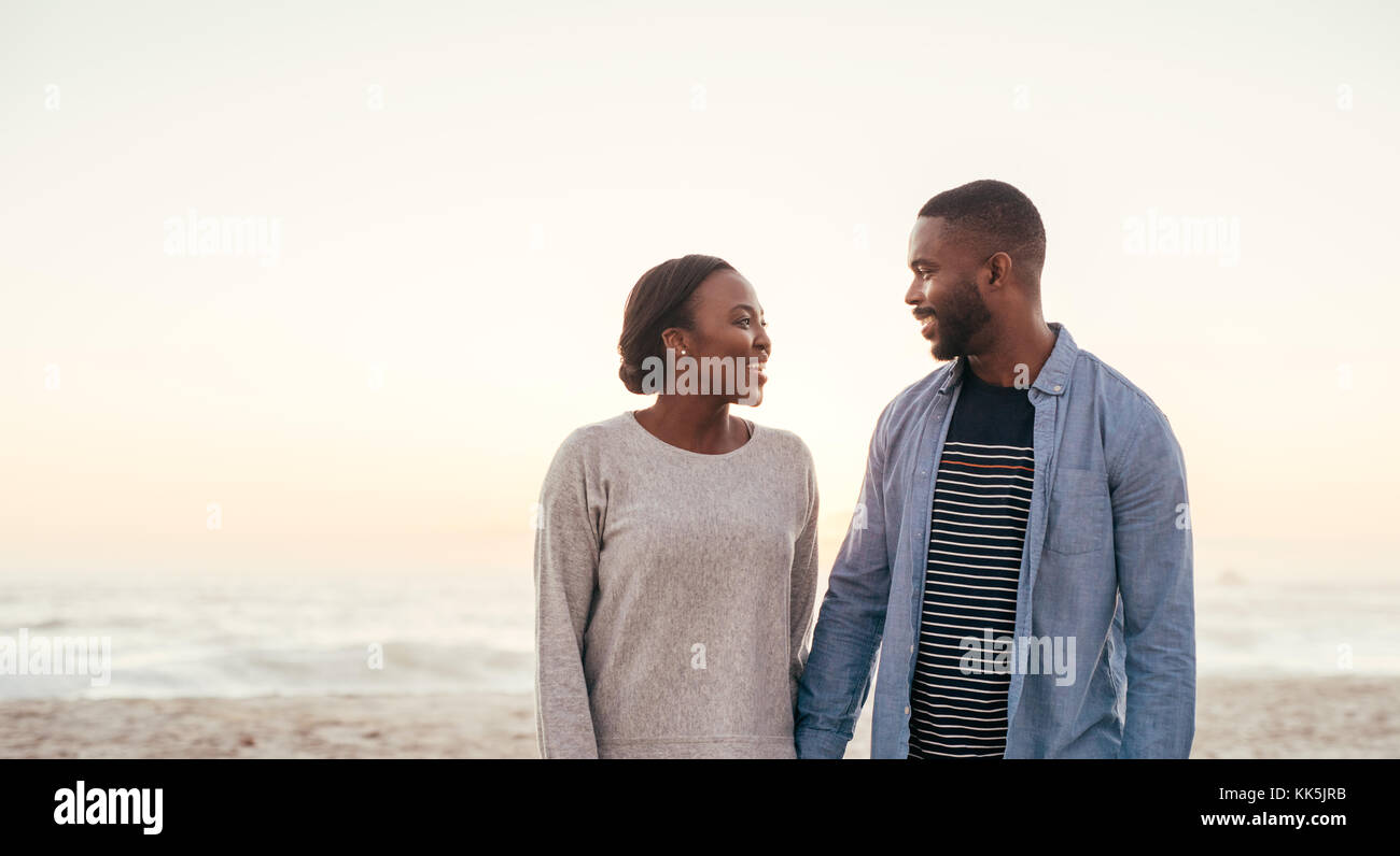 Lächelnd afrikanischen Paar hinunter einen Strand zusammen in der Dämmerung Stockfoto