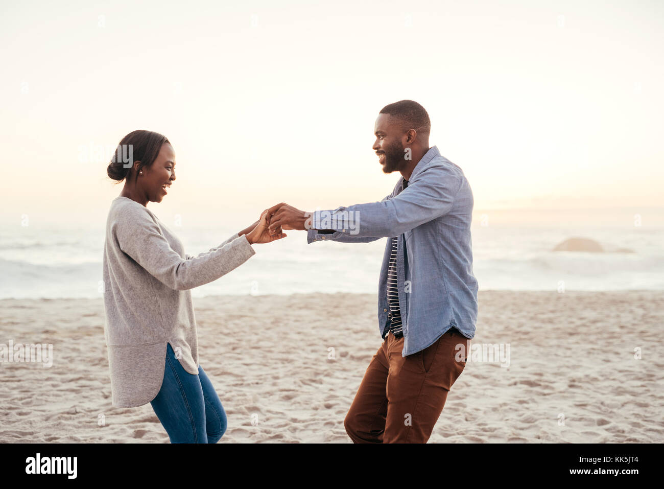 Lächelnden jungen afrikanischen Paar Tanz auf dem Strand bei Sonnenuntergang Stockfoto