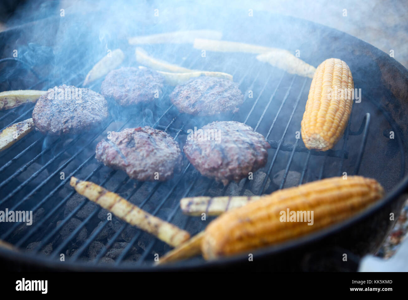 Rindfleischpastetchen und frische Maiskolben Grillen auf einen tragbaren Grill auf einem Campingplatz in der Nähe zu sehen. Stockfoto