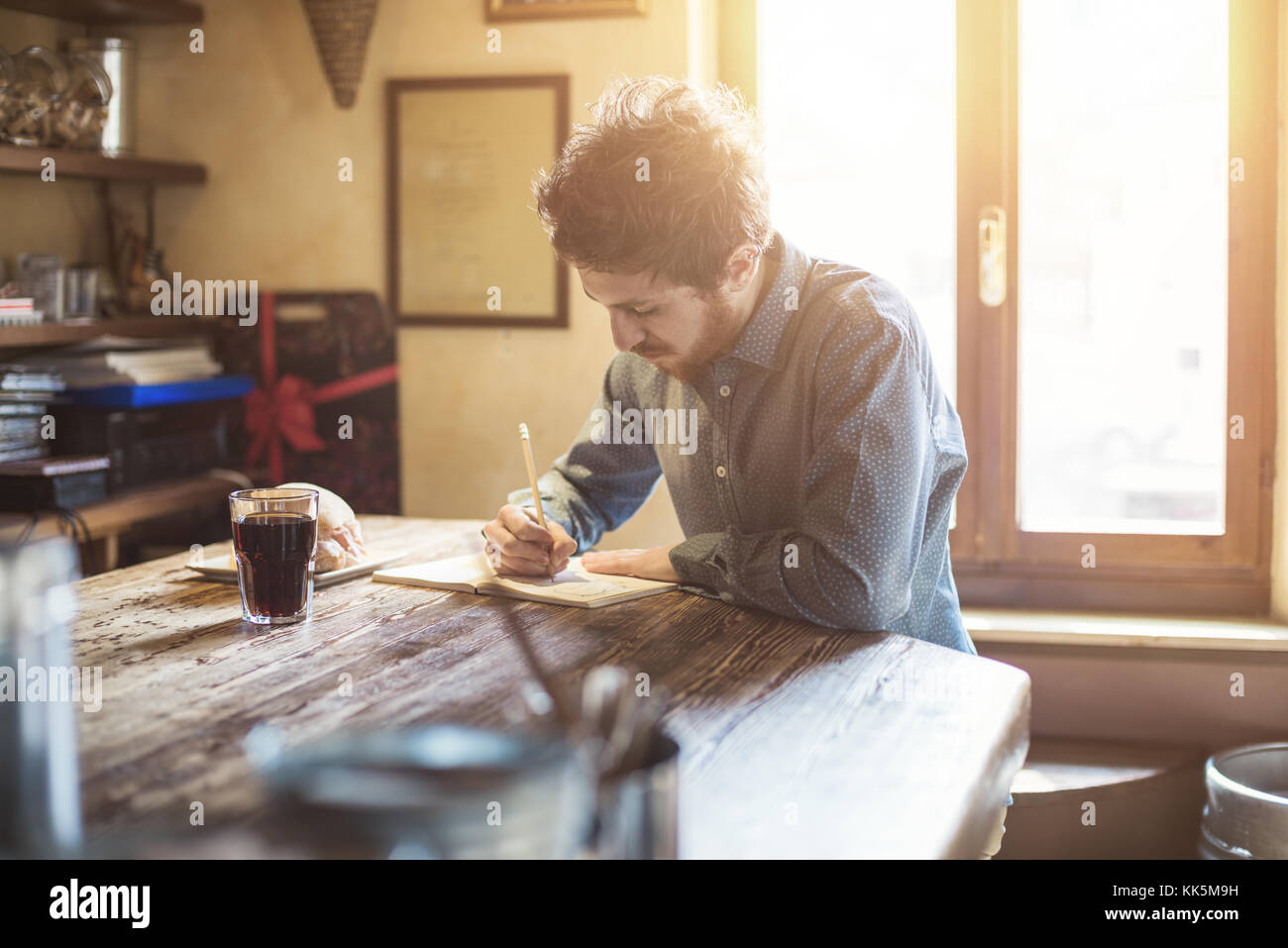 Junge hipster Mann Skizzieren auf einem Notebook mit einem rustikalen Holztisch während seiner Mittagspause Stockfoto