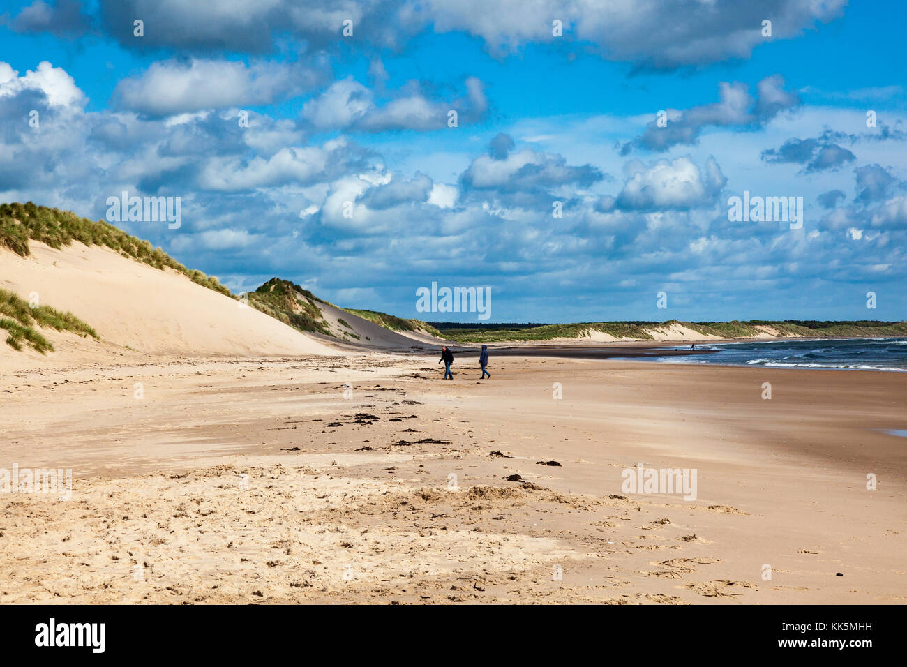 Ein paar Gehminuten am Strand an einem kalten Sommer Tag an der Druridge Bay, Northumberland, Großbritannien. Die Sonne scheint auf die Dünen Stockfoto