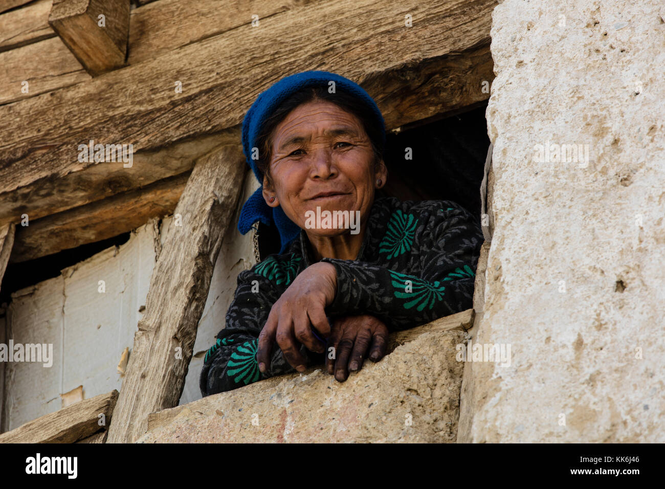 Eine Frau lächelt von ihrem Fenster in Nyerak Dorf im ZANSKAR RIVER GORGE - Zanskar, Ladakh, Indien Stockfoto