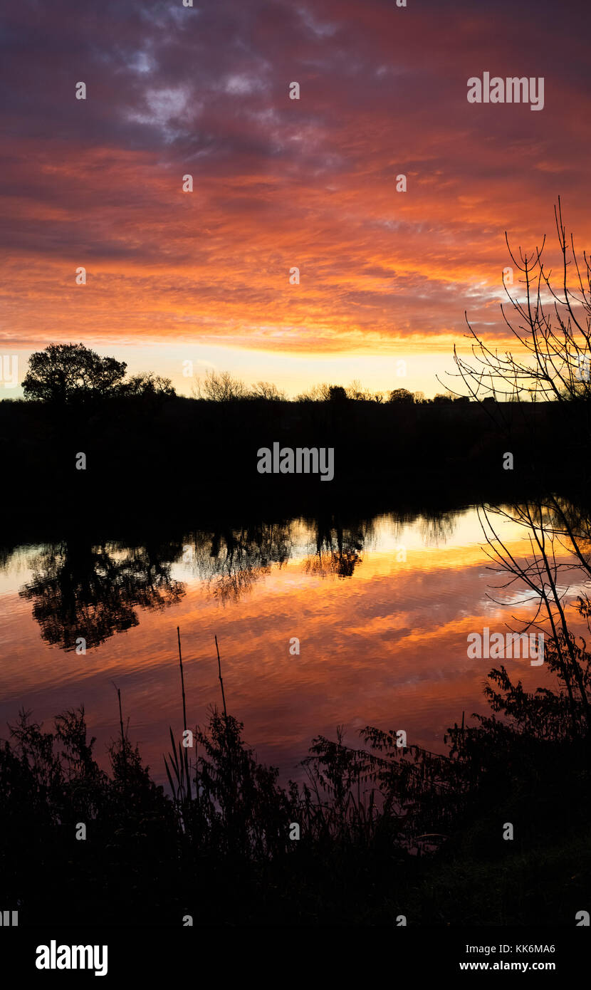 Sonnenaufgang und Baum Reflexionen über einen See in der Ortschaft Bourton auf dem Wasser. Cotswolds, Gloucestershire, England Stockfoto