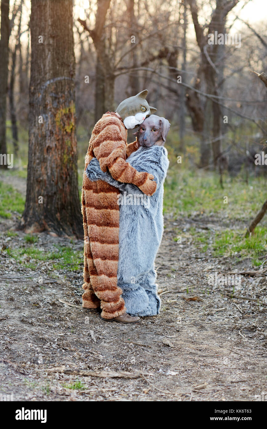 Volle Länge des Ein lustiges Paar in Liebe umarmen beim Tragen von Katze und Hund Karneval Kostüme draußen im Wald Stockfoto