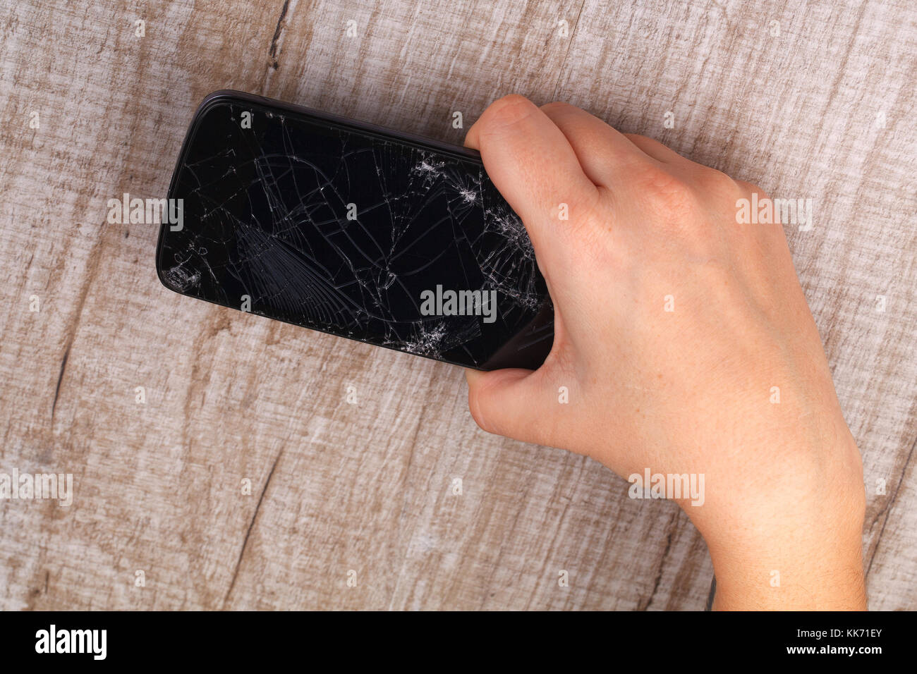 Ein Smartphone mit einem defekten Bildschirm in der Hand des Mädchens auf einem Holztisch. Close-up. Studio Beleuchtung. Stockfoto