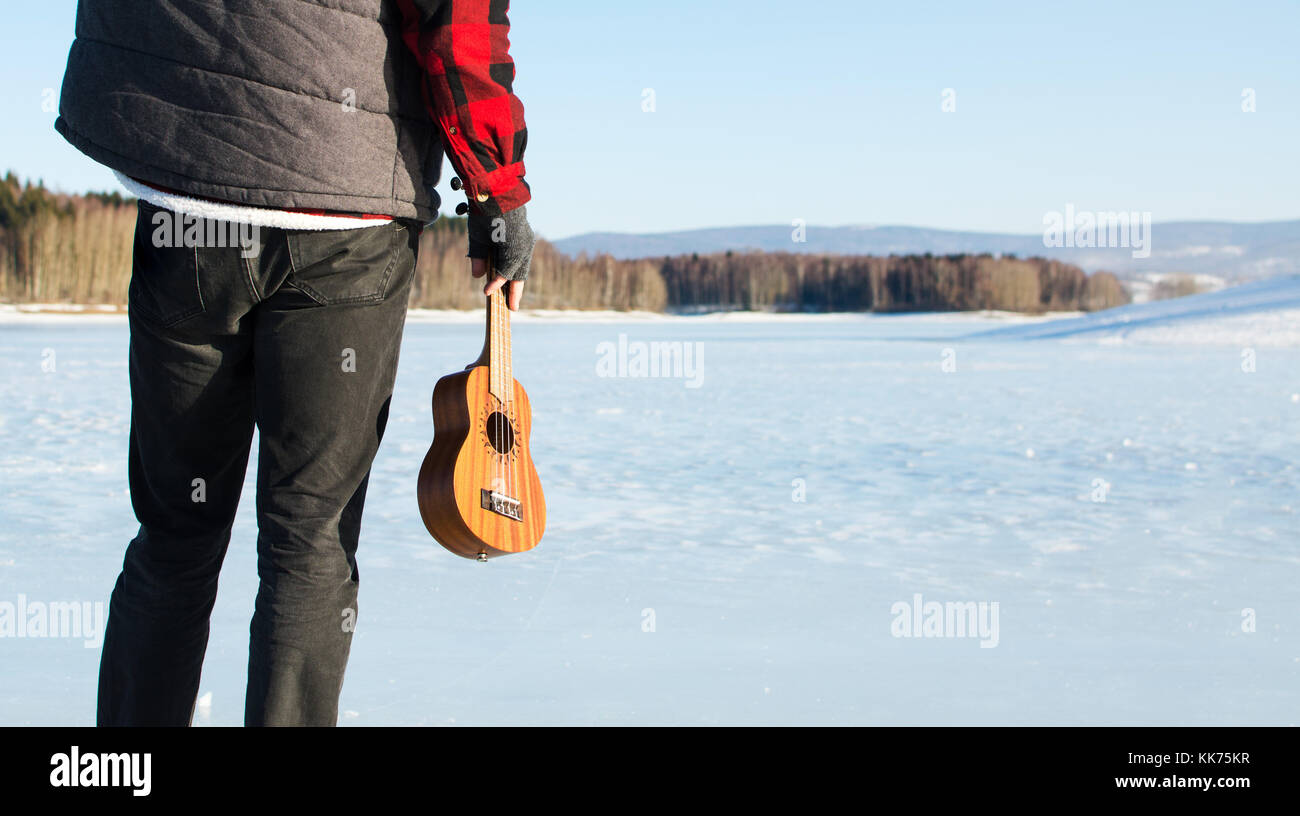 Mann mit Ukulele, stehend auf einem zugefrorenen See Stockfoto