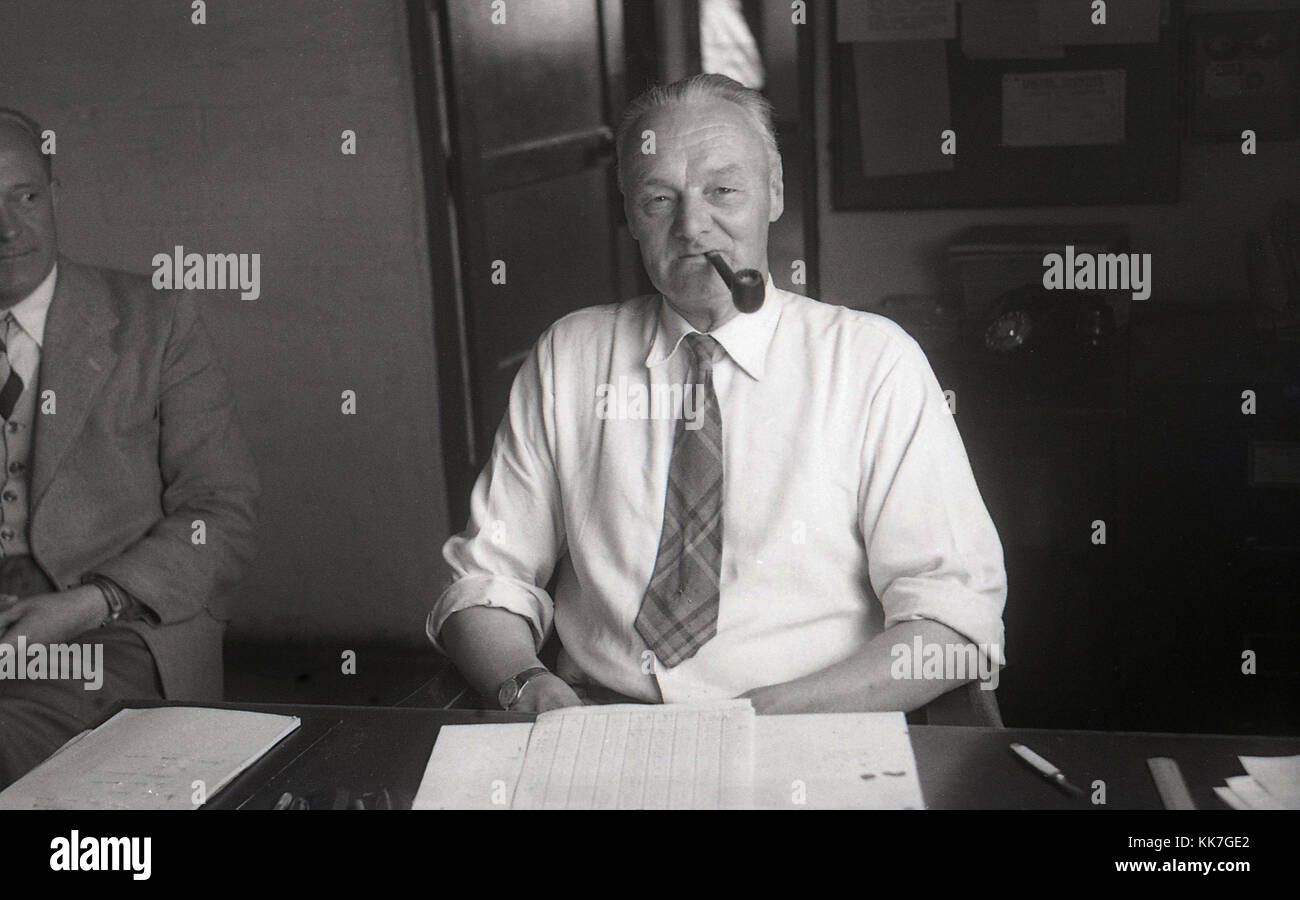 1950er Jahre, historische Bild zeigt einen Rang der Mensch in seinem Hemd und Krawatte sitzt an seinem Schreibtisch in einem Büro mit ein Rohr in den Mund. Mit einem Rohr ist eine traditionelle Form des Rauchens Tabak und war beliebt bei erwachsenen Männern in Großbritannien zu dieser Zeit. Stockfoto