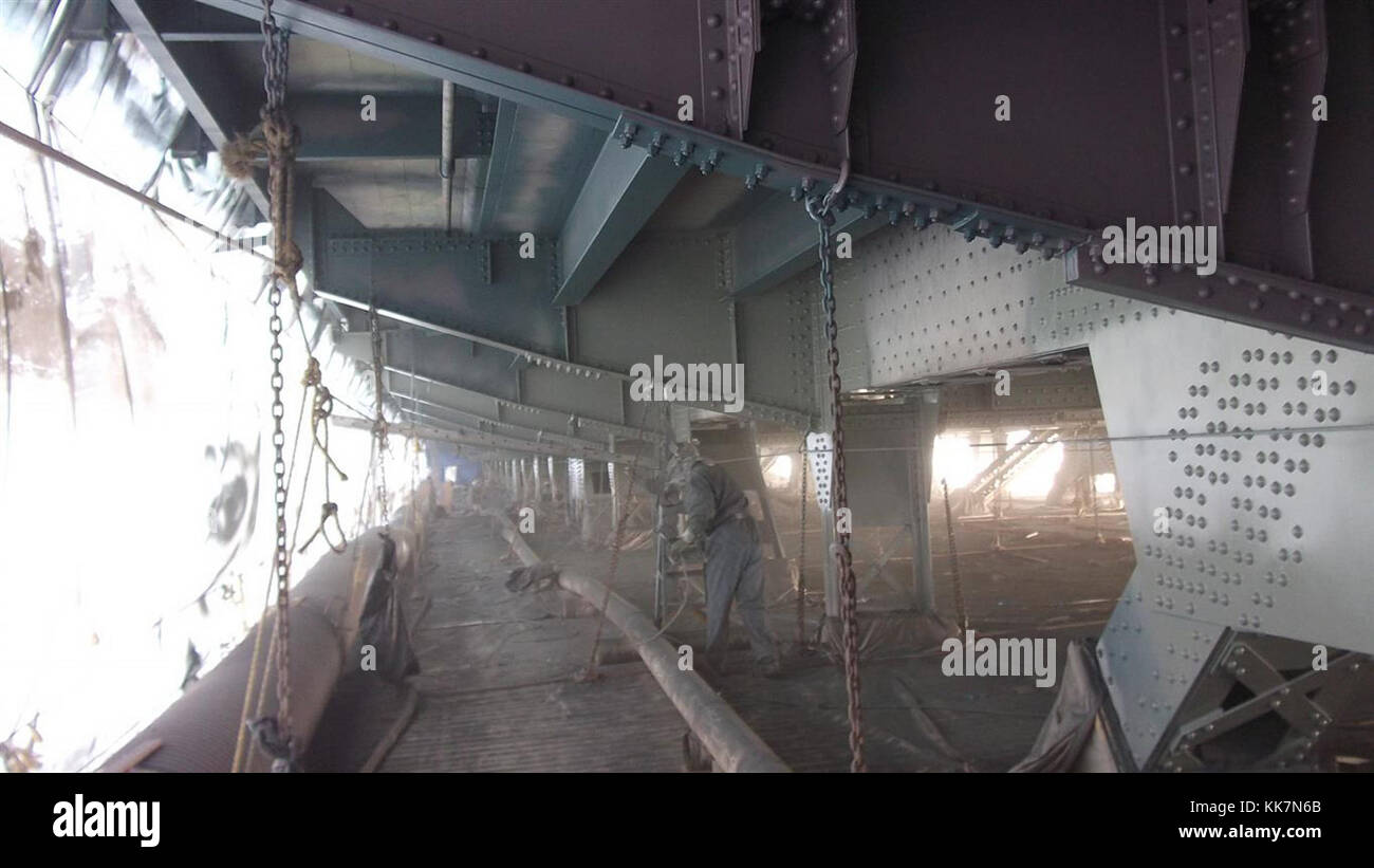 Unter der SR 99 Aurora Avenue Bridge in Seattle trägt ein Arbeiter den letzten Decklack auf Teile der Brücke auf. An dieser Stelle haben die neu lackierten Bereiche vier Schichten Grundierung. Das Grau ist eine normale Grundierung, während das Dunkelgrün als Streifenmantel bezeichnet wird. Die Streifenbeschichtung wird auf Kanten, Schweißnähte, Verbindungselemente und andere Bereiche aufgetragen, in denen flüssige Beschichtungen beim Trocknen zu dünn oder wegfließen. Die Streifenbeschichtung hilft beim Aufbau einer ausreichenden Korrosionsschutzschicht. Im Jahr 2016 bemalten die Besatzungen Teile der Brücke als Teil der laufenden Bemühungen von WSDOT, die Struktur zu erhalten und ihre Lichtfarbe zu erweitern Stockfoto