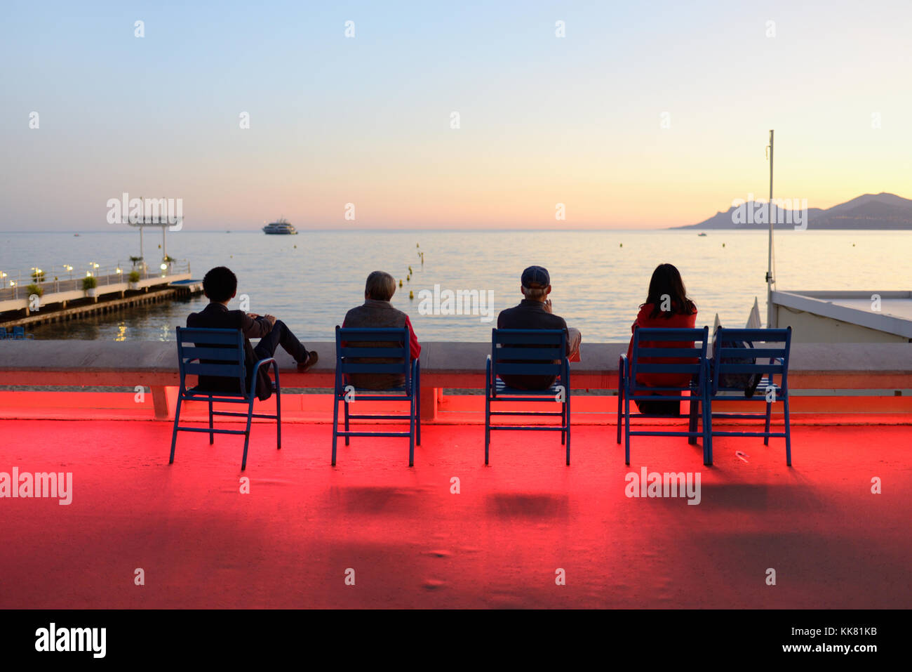 Vier Touristen genießen den Sonnenuntergang auf dem Boulevard de la Croisette, Cannes, bei Dusk, mit dramatischen Colour Street Lighting, Französisch Riviera, frankreich Stockfoto