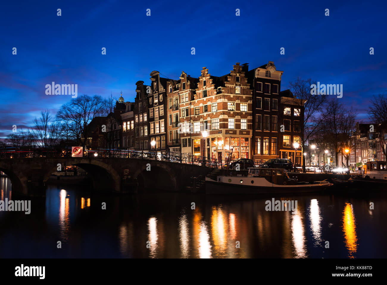 Typische Amsterdamer Gracht Häuser in historischer Architektur entlang der Grachten eine Brücke über das Wasser, in der Blauen Stunde der Dämmerung in Holland beleuchtet. Stockfoto