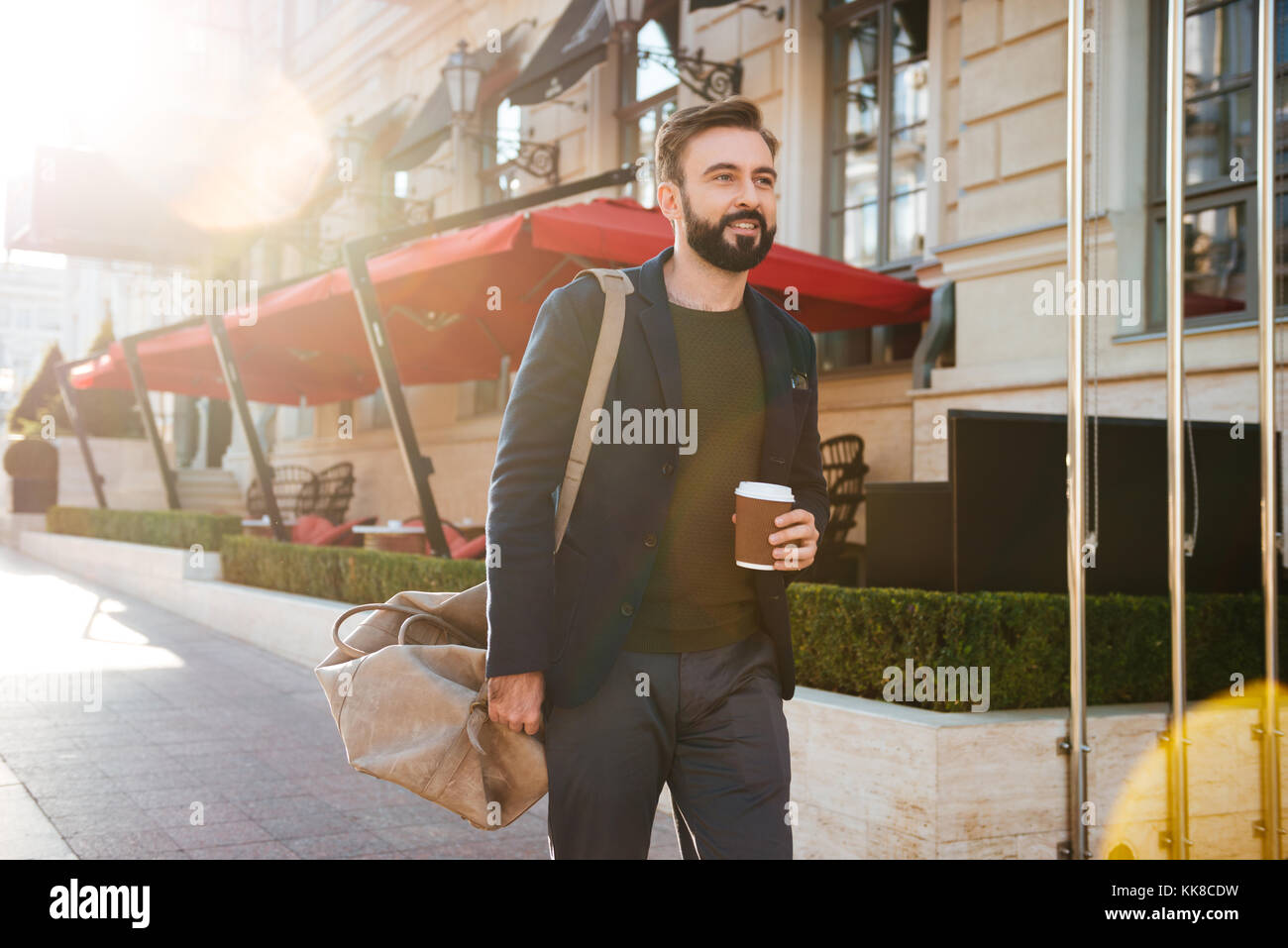 Porträt einer stattlichen lächelnden Mann Kaffee trinken während man auf einer Straße der Stadt und mit einer Tasche Stockfoto