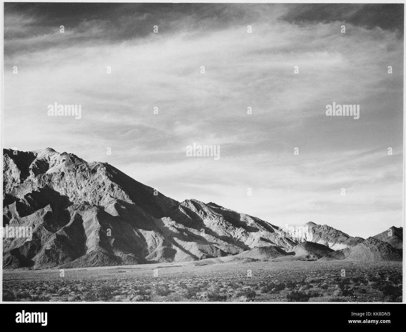 Eine schwarze und weiße Landschaft Foto aus dem Death Valley National Park, den flachen Boden führt zu den Rocky Mountain Peak im Hintergrund kurz Wüste Pflanzen bedeckt ist, wird das Bild stammt aus einer Serie von Fotografien bekannt als das Wandbild Projekt von Ansel Adams, er durch den National Park Service 1941 beauftragt wurde, eine fotografische Wandbild für das Ministerium des Innern in Washington DC zu erstellen, wird das Projekt zu einem Ende kam wegen des Zweiten Weltkrieges, die ursprünglich als Death Valley National Monument im Jahre 1933 bezeichnete es in einem Nationalpark im Jahr 1994 wurde der Park umfasst Teile von Cal Stockfoto