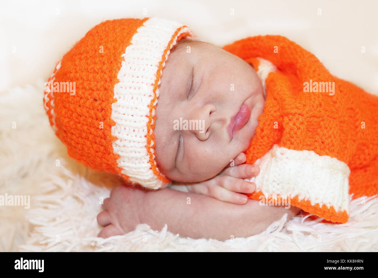 Cute friedlich schlafen neugeborene Baby in einen gestrickten orange Kostüm auf weiße Decke gekleidet. Stockfoto