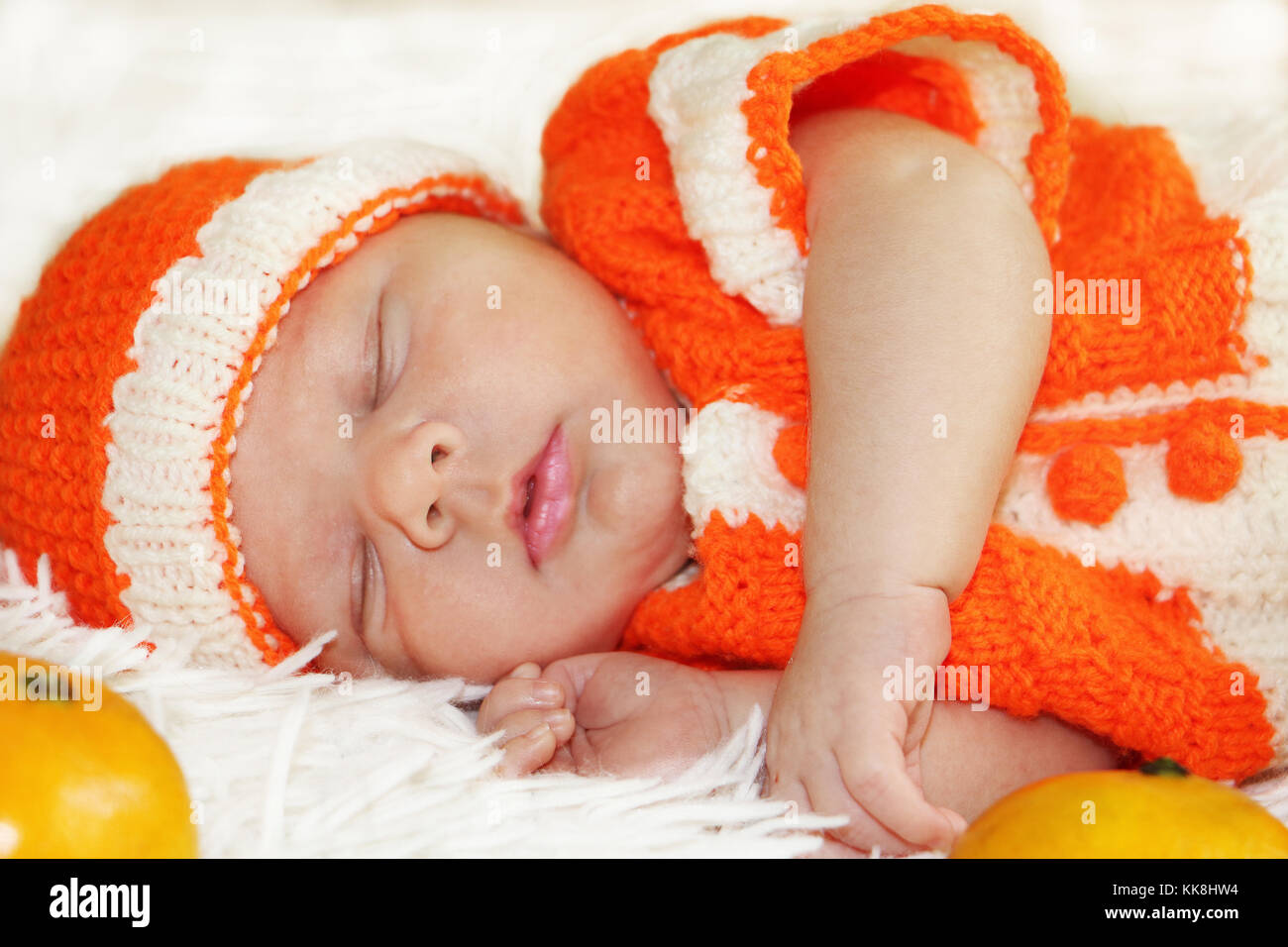 Cute friedlich schlafen neugeborene Baby in einen gestrickten orange Kostüm mit Orangen um ihm auf weißen Decke gekleidet. Stockfoto