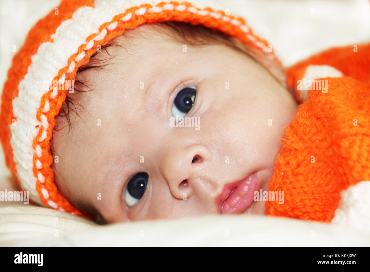 Nachdenklich Baby. Portrait von meditativen neugeborenes Baby mit wunderschönen blauen Augen in Orange aus Gewirken Kostüm auf weißem Fell Decke. Stockfoto