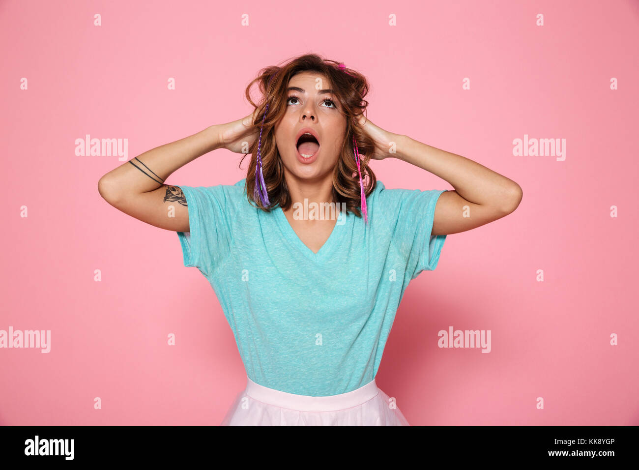 Nahaufnahme von schockiert hübsches Mädchen in mint Shirt halten Ihren Kopf nach oben suchen, auf rosa Hintergrund isoliert Stockfoto
