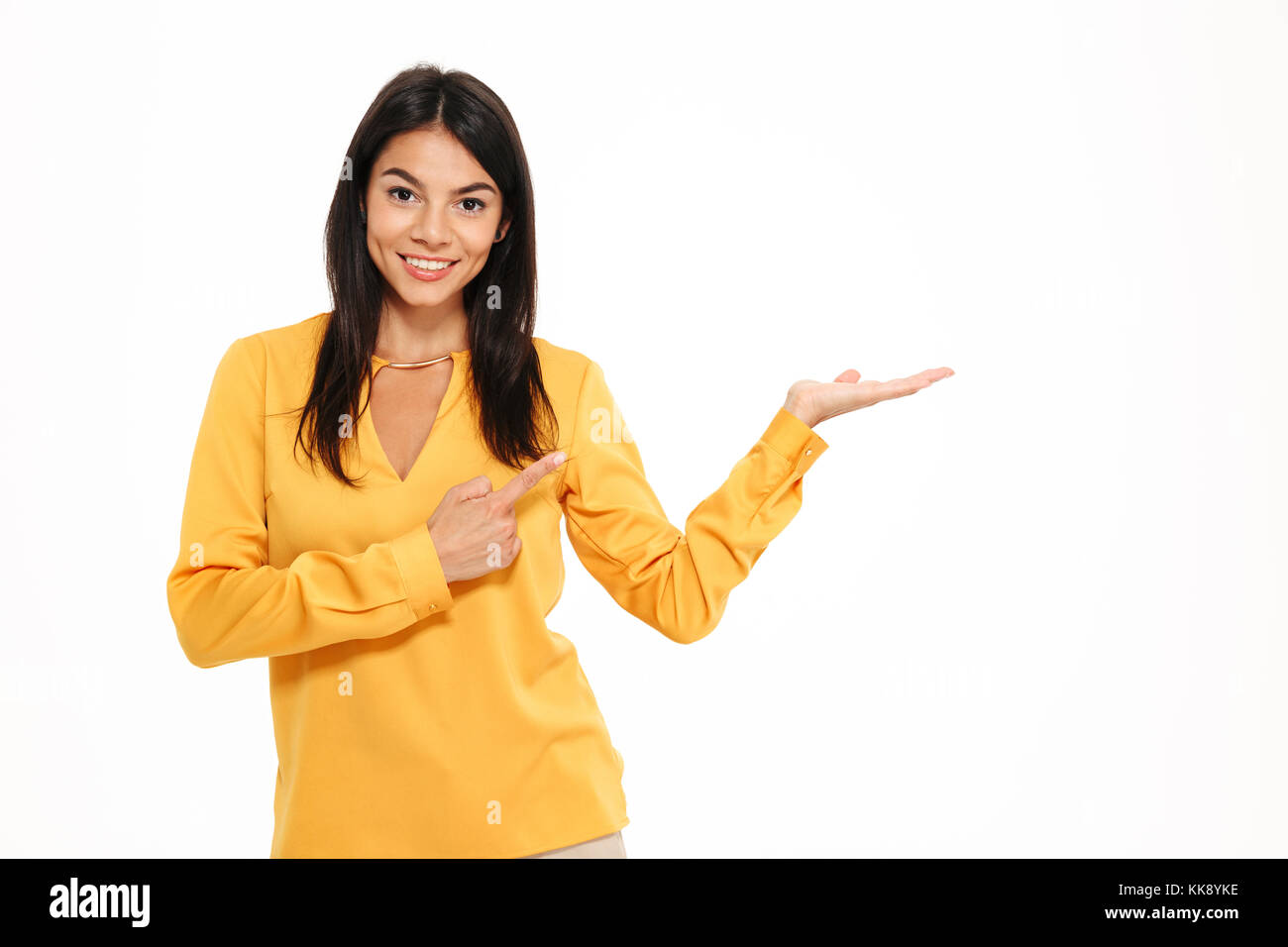 Bild fröhliche junge Dame im gelben Hemd, die auf weißem Hintergrund. Suchen Kamera holding Copyspace in der Hand und zeigen. Stockfoto