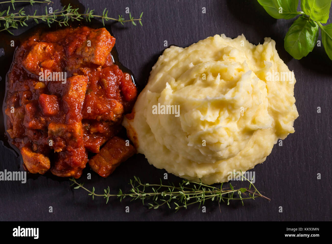 Schweinefleisch Eintopf in Tomatensauce mit Kartoffelpüree und Kräuter Stockfoto