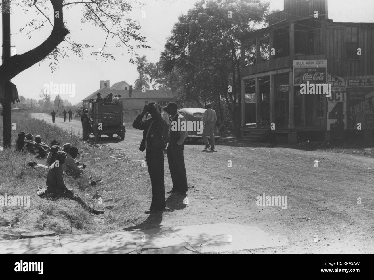 Schwarz-weiß Fotografie afroamerikanische Männer an der Seite eines Feldweg ruhend, Autos auf der Straße, kleine Unternehmen im Hintergrund, Belzoni, Mississippi, November, 1939. Von der New York Public Library. Stockfoto