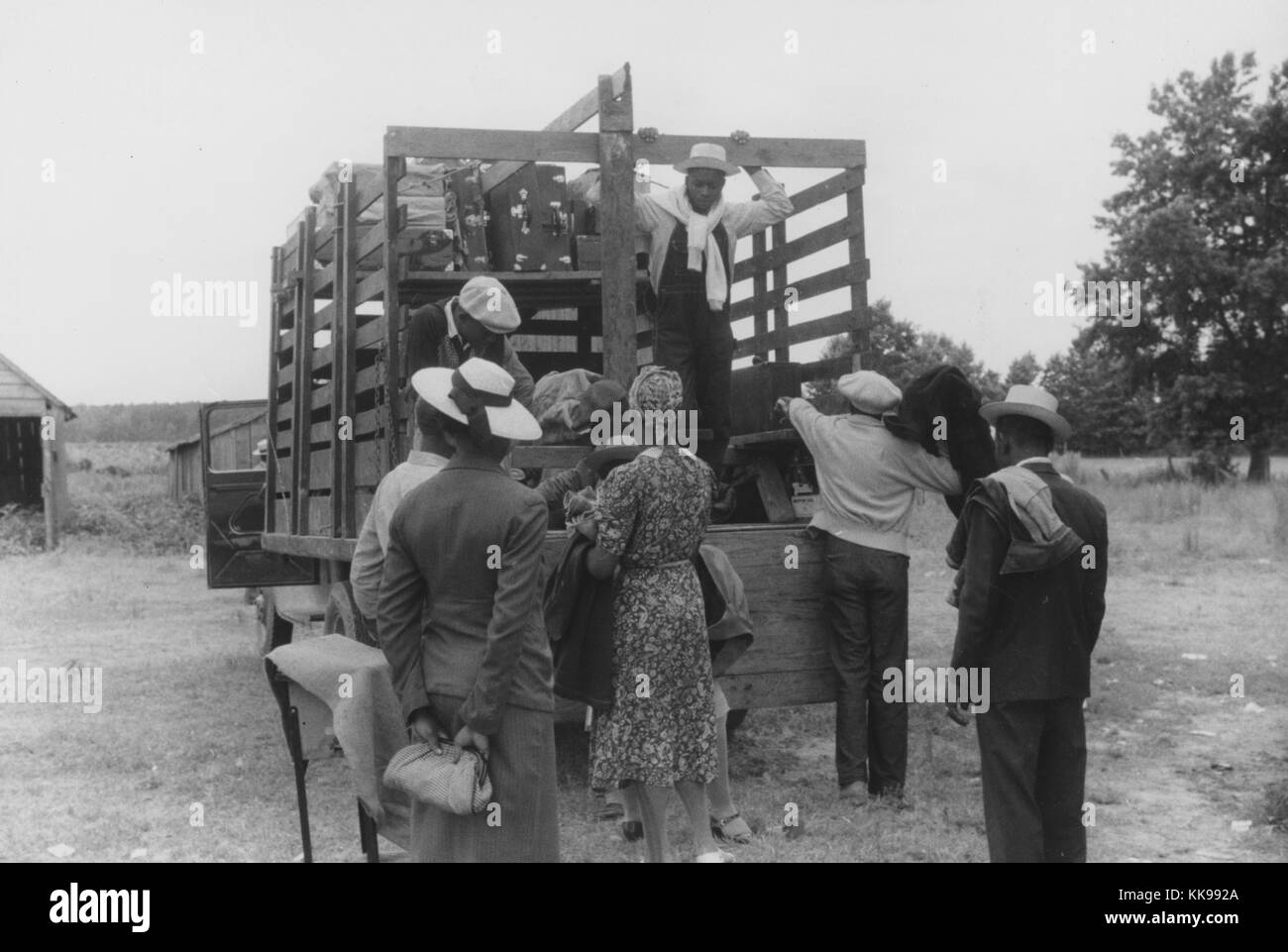 Ein Foto von Migrant farm workers Beladen eines Lkw mit ihren Habseligkeiten, das Bett des Staplers mit Regalen ausgestattet wurde, die die Breite des Fahrzeugs ihr Gepäck Overhead zu halten, Bänke aufgebaut wurden, für das Volk, die Arbeiter sind in Jacken, Hosen und Kleider gekleidet, wie sie Reisen nach Einziges, Virginia aus North Carolina Belcross werden landwirtschaftliche Arbeit zu suchen, 1940. Von der New York Public Library. Stockfoto