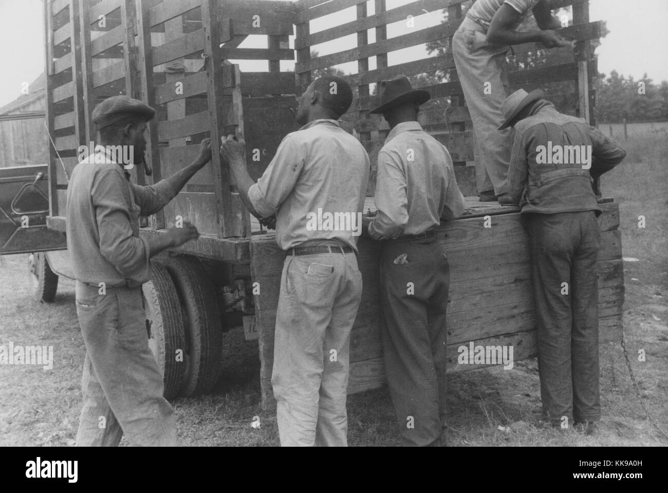 Ein Foto von einer Gruppe von Migranten die Bauern, die auf einem Lkw, Sie bereiten sich für Reisen nach Einziges, Virginia, die Männer sind alle Tragen von Hosen und Shirts oder Jacken, während Sie auf dem Bett des Lkw, Belcross arbeiten, Nord-Carolina, Juli 1940. Von der New York Public Library. Stockfoto