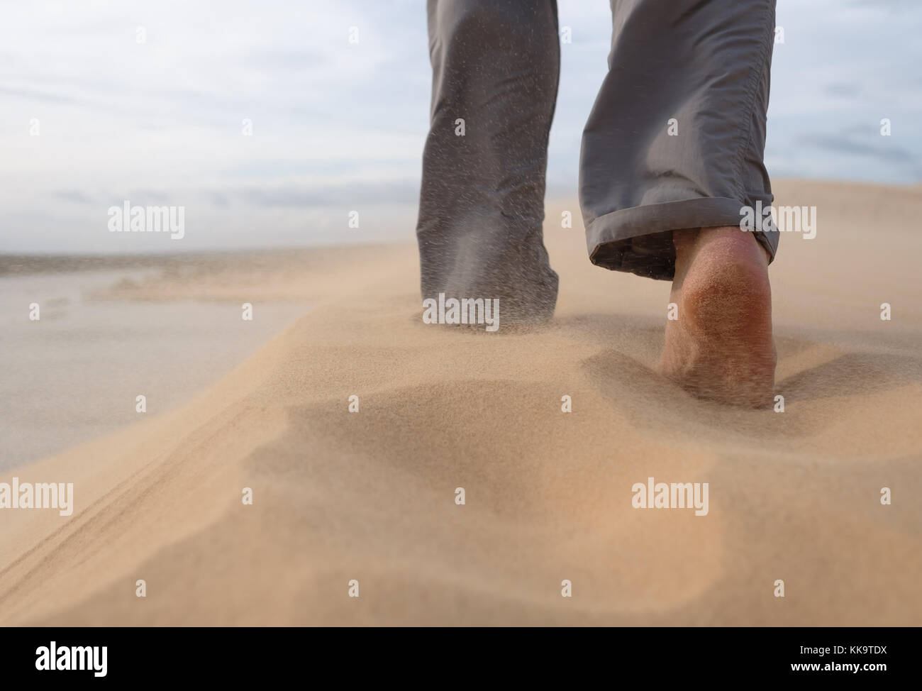 Ein Mann Spaziergänge entlang der Sandstrand. In der Luft, der Sand fliegt von einem starken Wind. Stockfoto