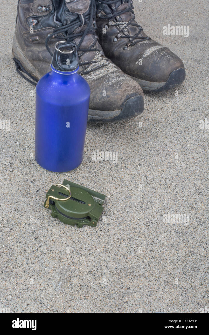 Trekking Stiefel, blau Wasserflasche und Kompass - als Metapher für das Reisen und Wandern in der Wüste oder ariden Zonen. Stockfoto