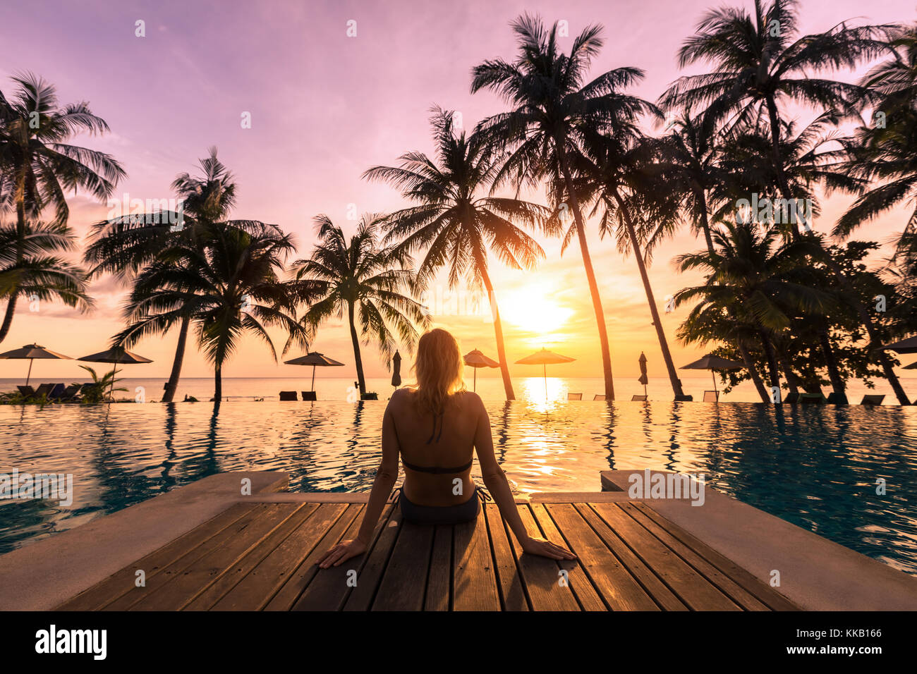 Frau am Pool in einem luxuriösen Hotel Resort direkt am Strand bei Sonnenuntergang geniessen Sie perfekten Strand Urlaub Stockfoto
