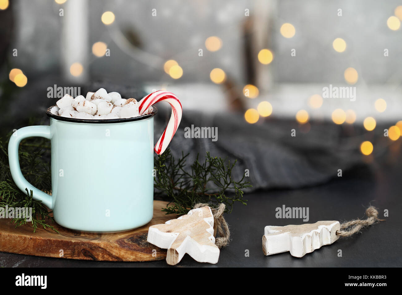 Emaille Tasse heißen Kakao trinken mit Marshmallows und Candy Cane gegen eine rustikale Hintergrund mit schönen Bokeh Lichter vor einem Fenster. Holz chri Stockfoto