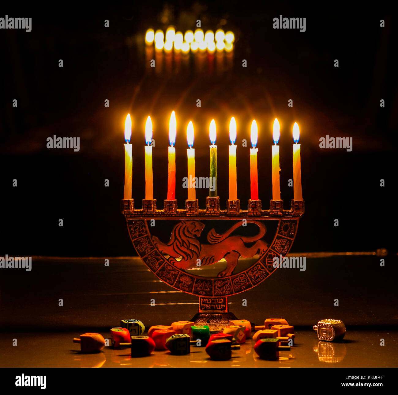 Hanukkah Menorah mit brennenden Kerzen auf dem Tisch sitzt; die Lichter spiegeln sich in den dunklen Fenster über ihnen; dreidels auf dem Tisch vor o verstreut Stockfoto