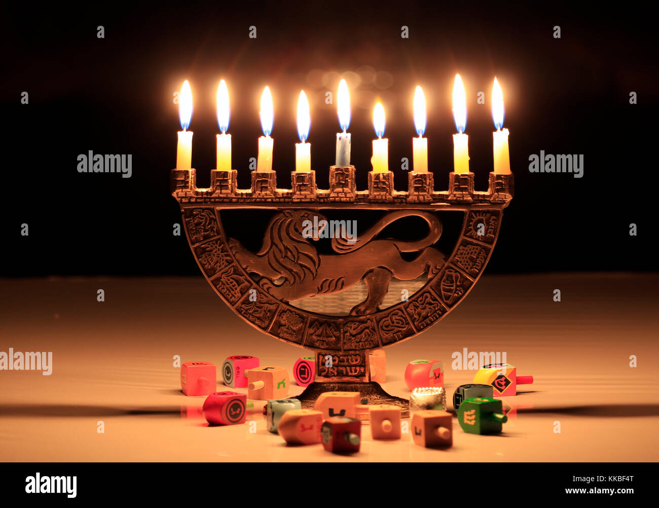 Hanukkah Menorah mit brennenden Kerzen auf dem Tisch sitzt; die Lichter spiegeln sich in den dunklen Fenster hinter Ihnen; dreidels auf dem Tisch vor o verstreut Stockfoto