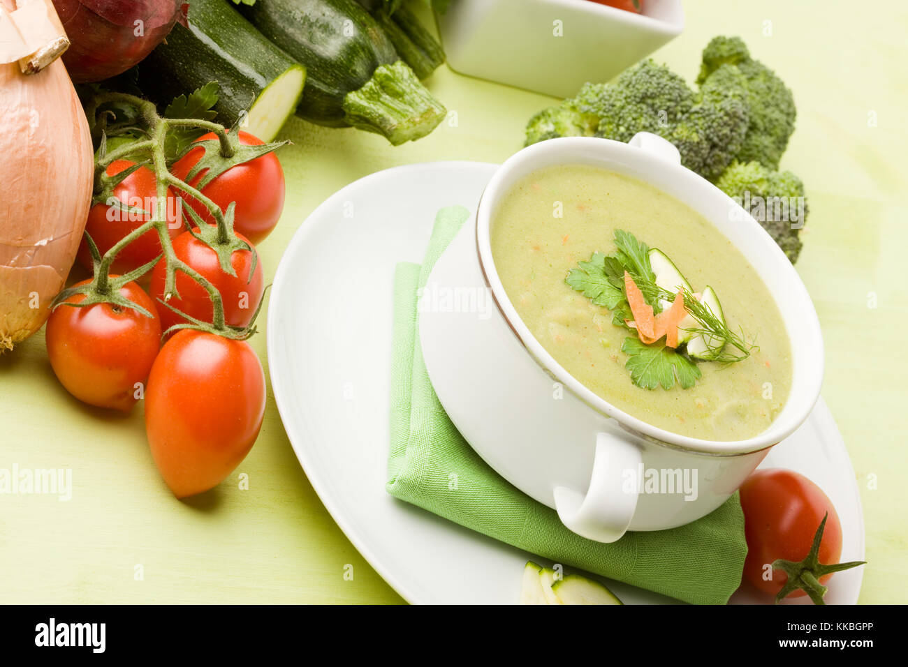 Foto von vegetarische Gemüsesuppe am grünen Tisch aus Holz mit verschiedenen Gemüsen arround Stockfoto